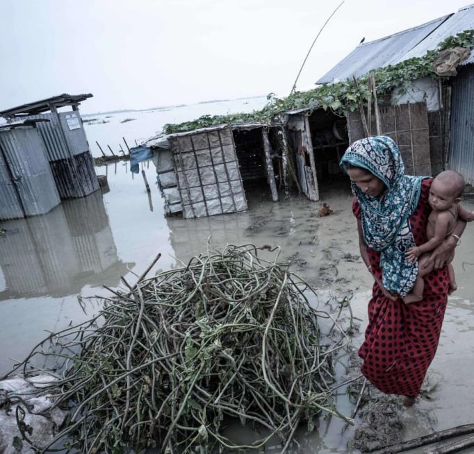 A woman holding a baby walking in a flooded soil